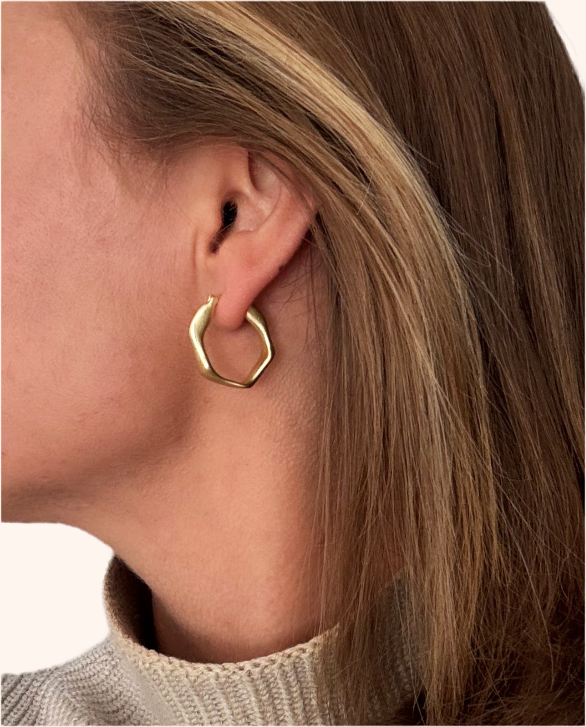 Gold hoop earring worn by a person with a neutral background